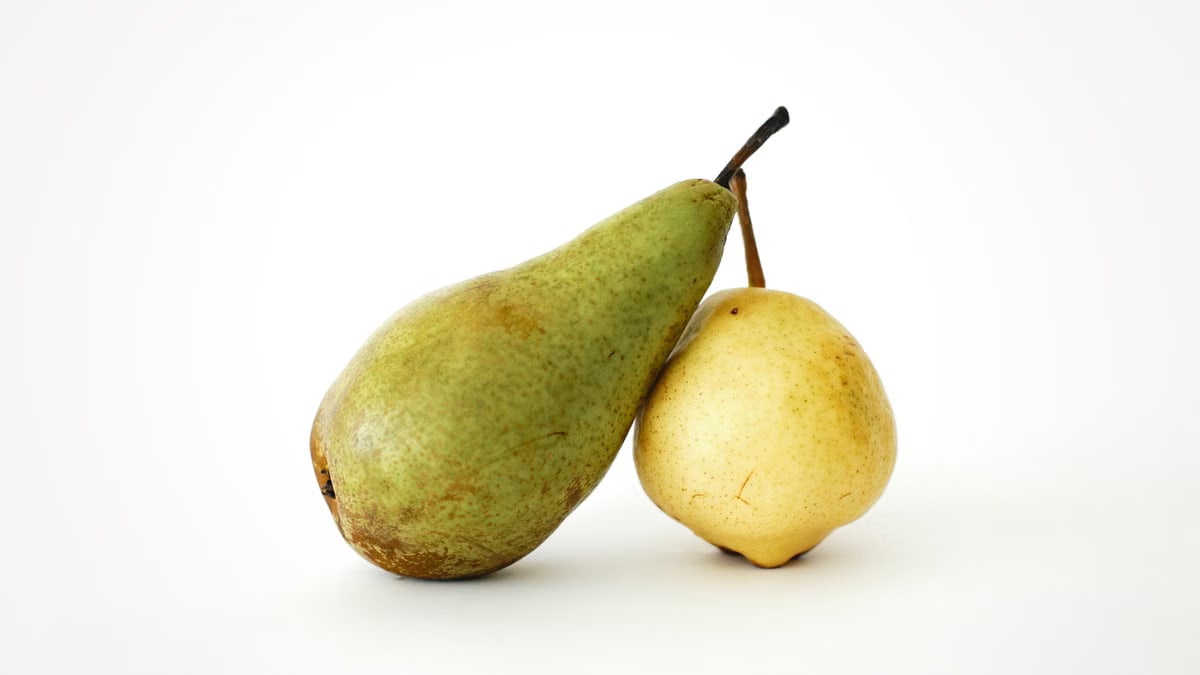 Two ripe pears, one green and one yellow, on a white surface conveying freshness.